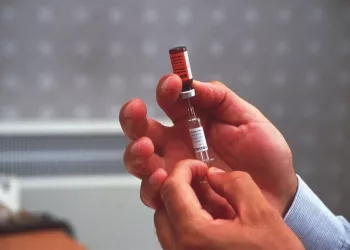 Vaccine. Doctor preparing a measles vaccine. He is using a hypodermic syringe to dissolve the powdered vaccine (vial, upper centre) with a solvent. Vaccination against measles in childhood can provide long-term protection. The injection of components of the virus particle causes the response of the immune system to be stronger when measles infections occur in the future., Image: 102389811, License: Rights-managed, Restrictions: , Model Release: no, Credit line: Science Photo Library / Sciencephoto / Profimedia
