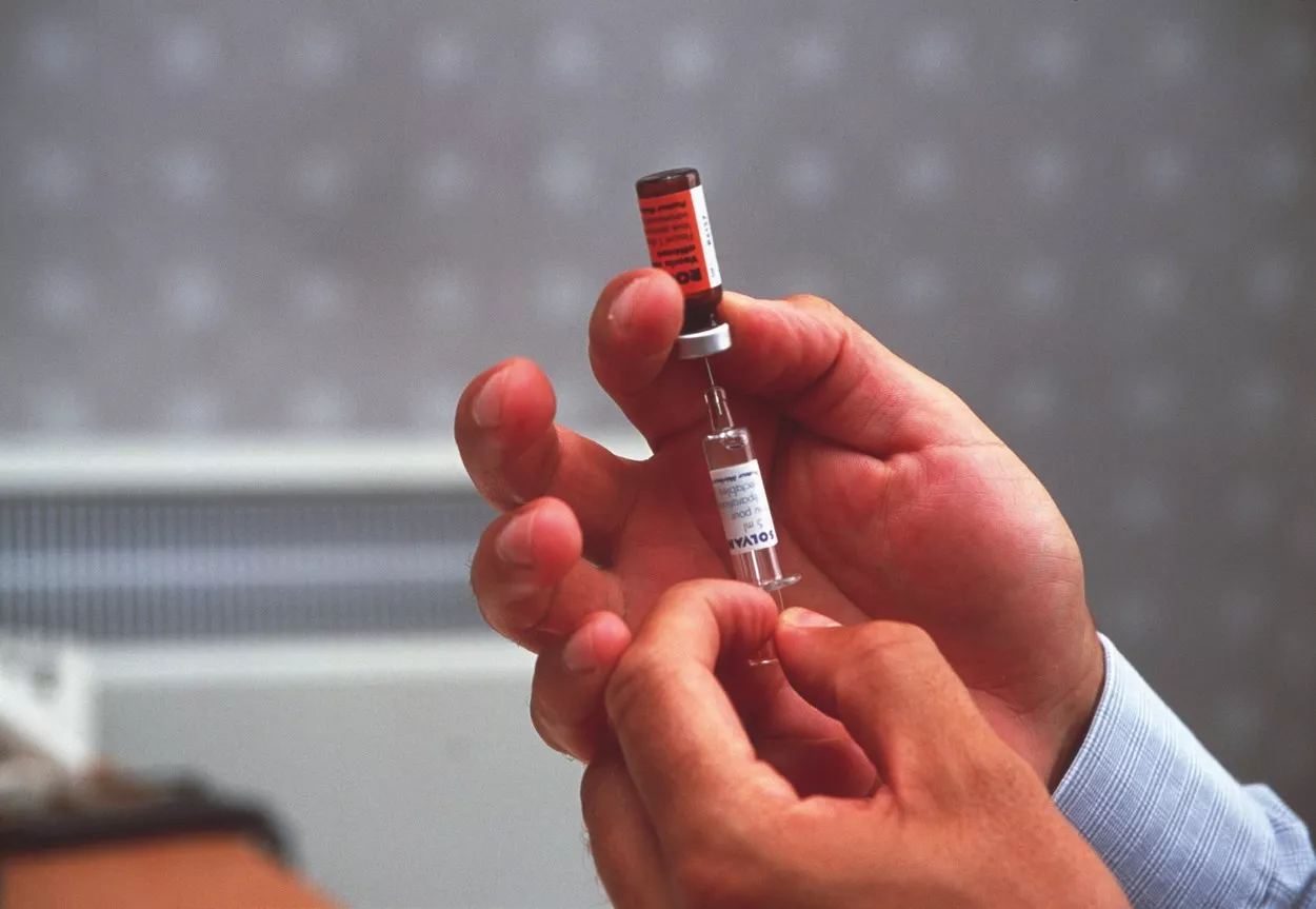Vaccine. Doctor preparing a measles vaccine. He is using a hypodermic syringe to dissolve the powdered vaccine (vial, upper centre) with a solvent. Vaccination against measles in childhood can provide long-term protection. The injection of components of the virus particle causes the response of the immune system to be stronger when measles infections occur in the future., Image: 102389811, License: Rights-managed, Restrictions: , Model Release: no, Credit line: Science Photo Library / Sciencephoto / Profimedia