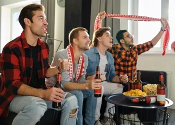 Excited football fans with drinks and food having fun by watching football match at home