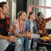 Excited football fans with drinks and food having fun by watching football match at home