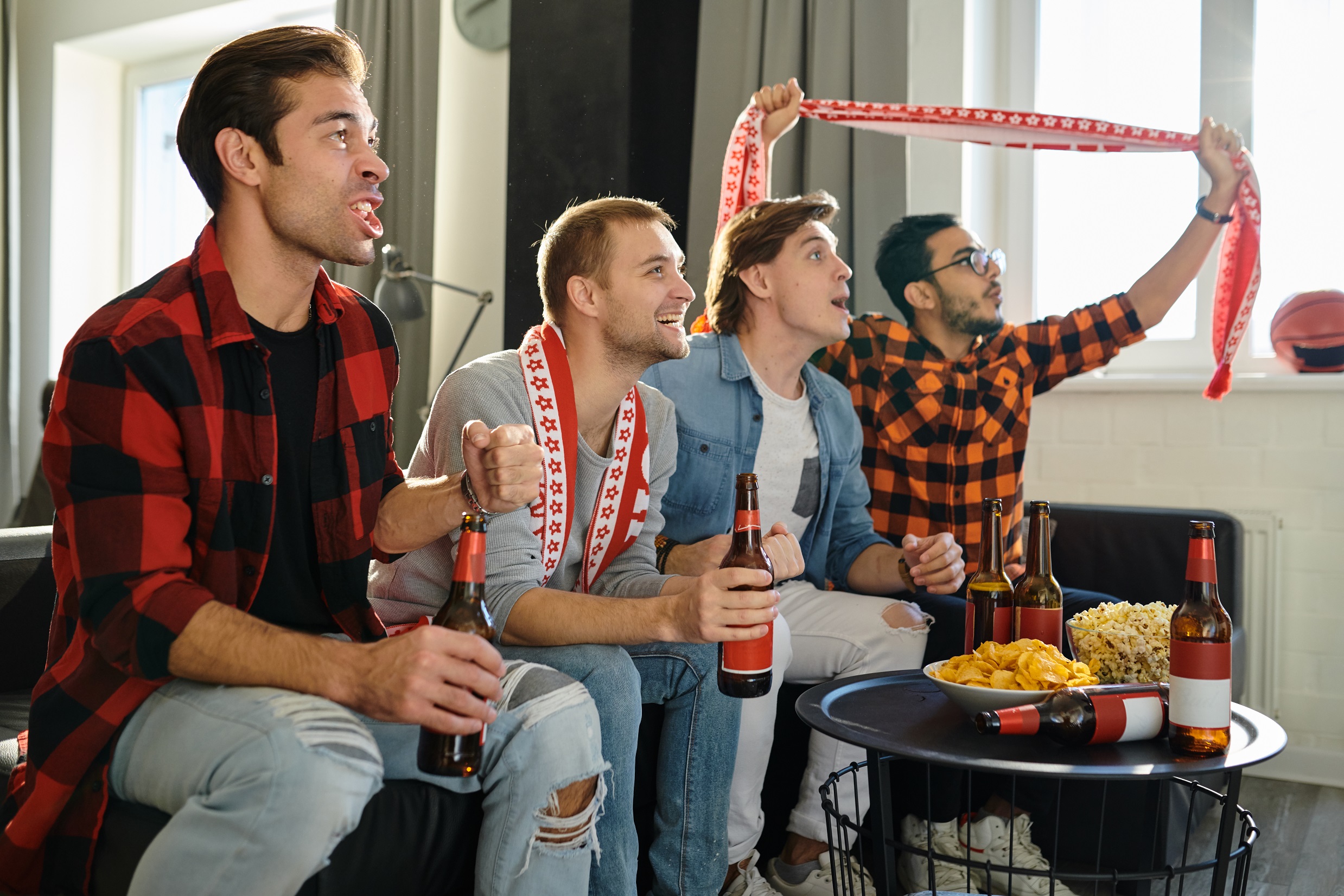 Excited football fans with drinks and food having fun by watching football match at home