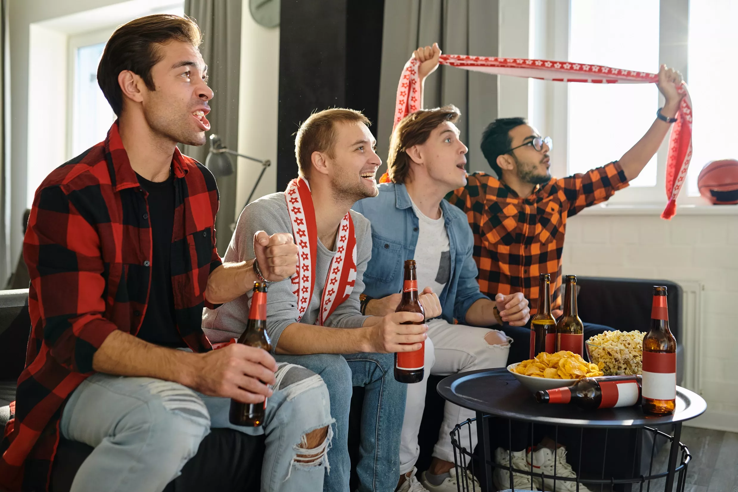Excited football fans with drinks and food having fun by watching football match at home