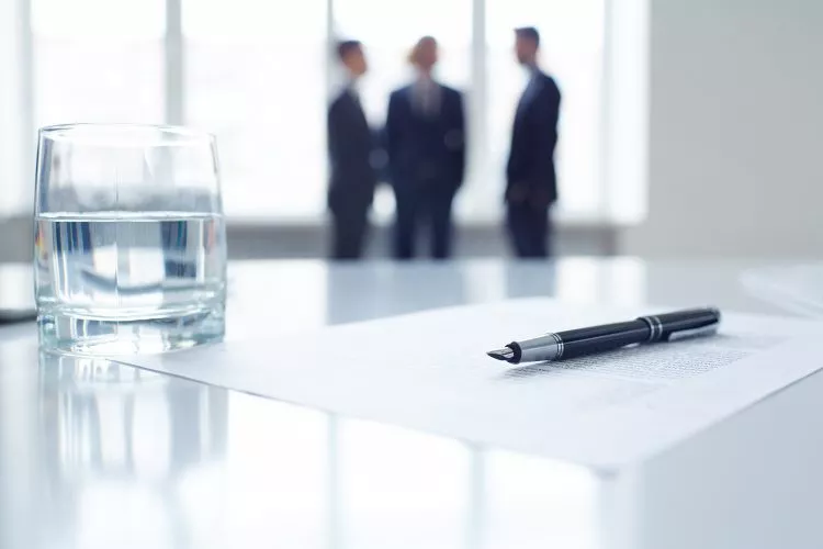 Image of business document, pen and glass of water at workplace with group of colleagues on background