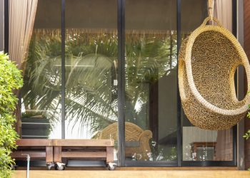 A wicker armchair in the form of a cocoon suspended on the terrace. The recreation scene, the concept of travel and recreation