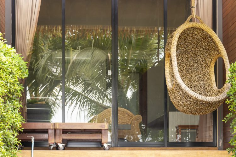 A wicker armchair in the form of a cocoon suspended on the terrace. The recreation scene, the concept of travel and recreation