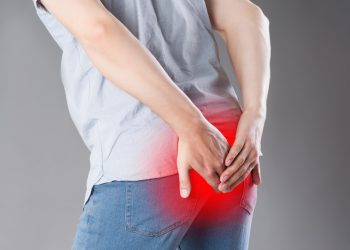 Man suffering from hemorrhoids, anal pain on gray background, painful area highlighted in red