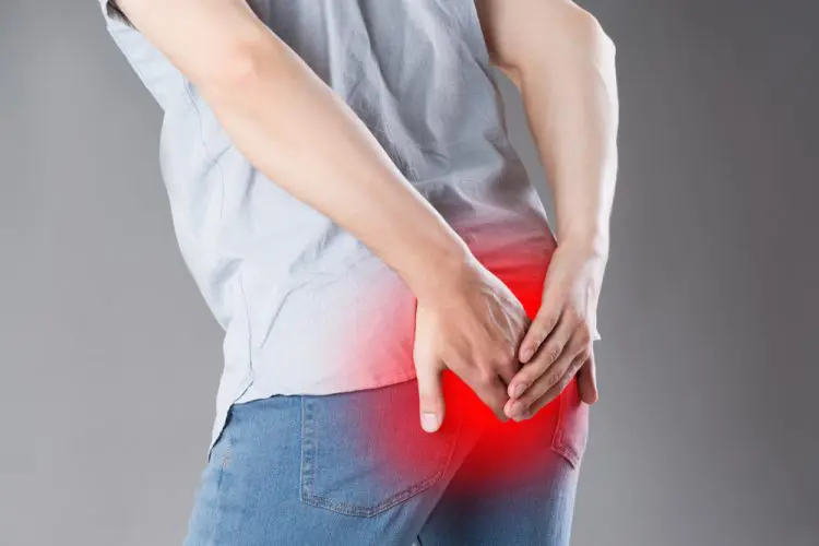 Man suffering from hemorrhoids, anal pain on gray background, painful area highlighted in red