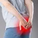 Man suffering from hemorrhoids, anal pain on gray background, painful area highlighted in red