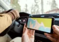 Hands of young woman sitting by driver and holding smartphone with map of the place where she and her husband travelling by car