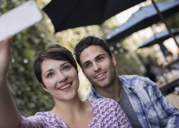 A couple seated at an outdoor city cafe, taking a selfy with a smart phone.
