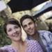 A couple seated at an outdoor city cafe, taking a selfy with a smart phone.