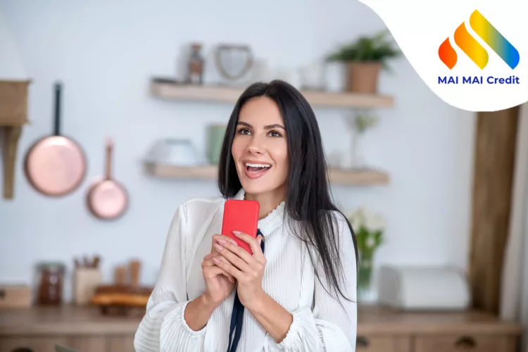 At home.Young woman in her kitechen, holding red smartphone, smiling excitedly