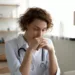 Close up thoughtful woman doctor with closed eyes sitting at work desk in hospital, meditating at workplace, female therapist physician gp wearing white coat uniform praying, asking help