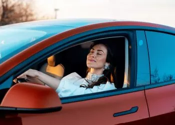 Close view of a woman smiling with closed eyes while sitting in a red parked car at sunset