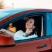 Close view of a woman smiling with closed eyes while sitting in a red parked car at sunset