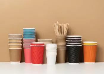 stacks of assorted disposable paper cups for drinks, coffee and tea on a white table. Takeaway beverage container