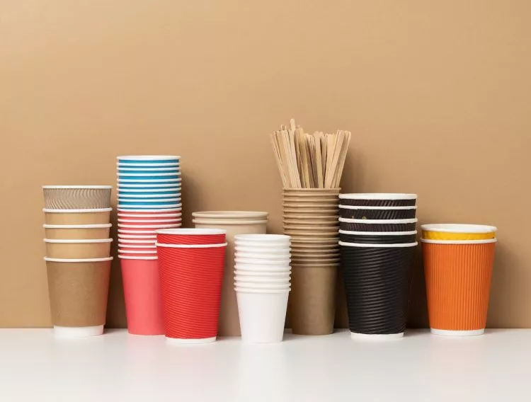 stacks of assorted disposable paper cups for drinks, coffee and tea on a white table. Takeaway beverage container